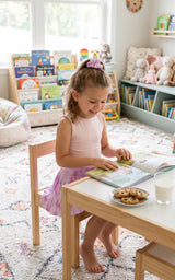 Little girl wearing a pink sleeveless tank and matching pleated skort, seated at a table with a pink scrunchie in her hair.