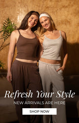 Two women posing in matching lounge sets in a warmly lit room with a textured gold wall, a curved sofa, and a potted plant. One set is dark brown and the other is light gray. Promotional text reads: "Refresh your style. new arrivals are here. shop now"