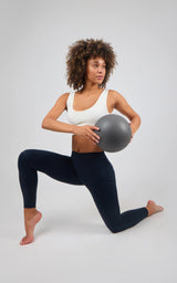 Woman wearing high-waisted, dark navy leggings with a matte finish, performing a lunge while holding a gray exercise ball.
