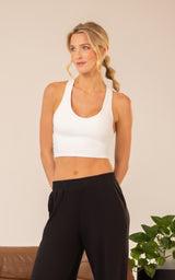 Woman wearing a white scoop-neck built-in bra bralette with wide straps and black high-waisted pants.